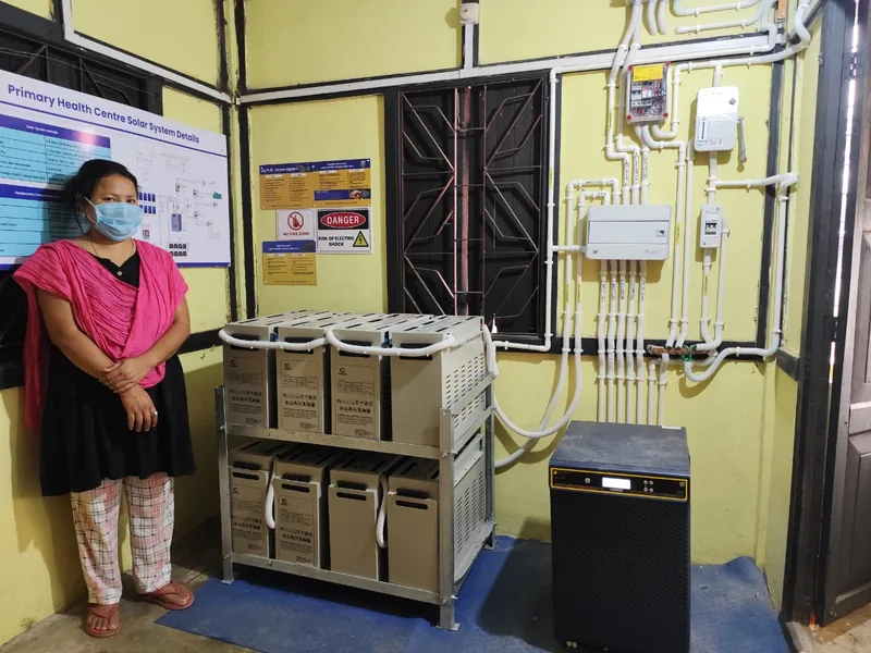 A masked health worker beside the solar battery backup installed at her facility