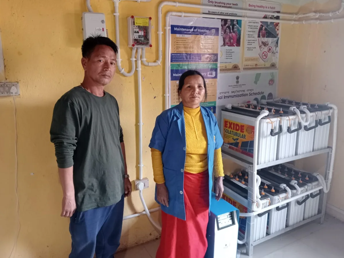 Two residents standing beside the battery bank of their off-grid solar system in Manipur