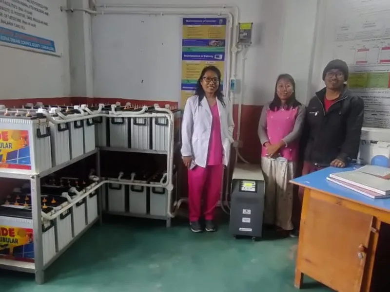 Health centre staff standing beside the solar battery bank and inverter powering their facility
