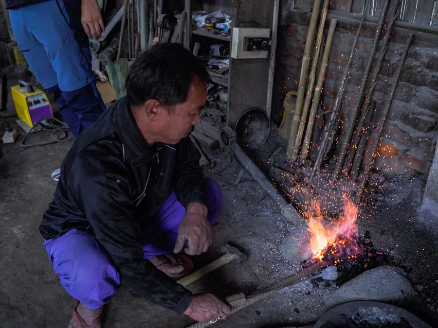 Blacksmith working at a forge driven by a solar-powered blower in Imphal
