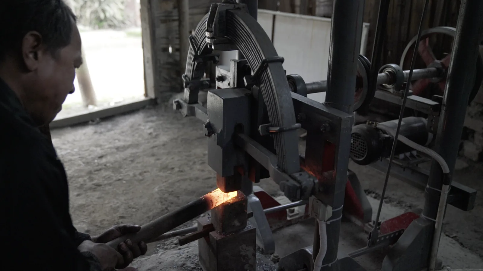 Blacksmith shaping hot iron under a solar-powered power hammer at Laingam Iron House, Imphal